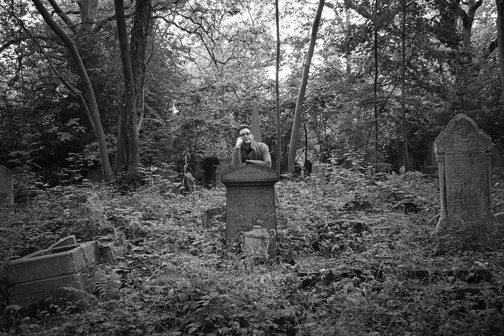 Sheldon K. Goodman standing among gravestones in a wooded cemetery